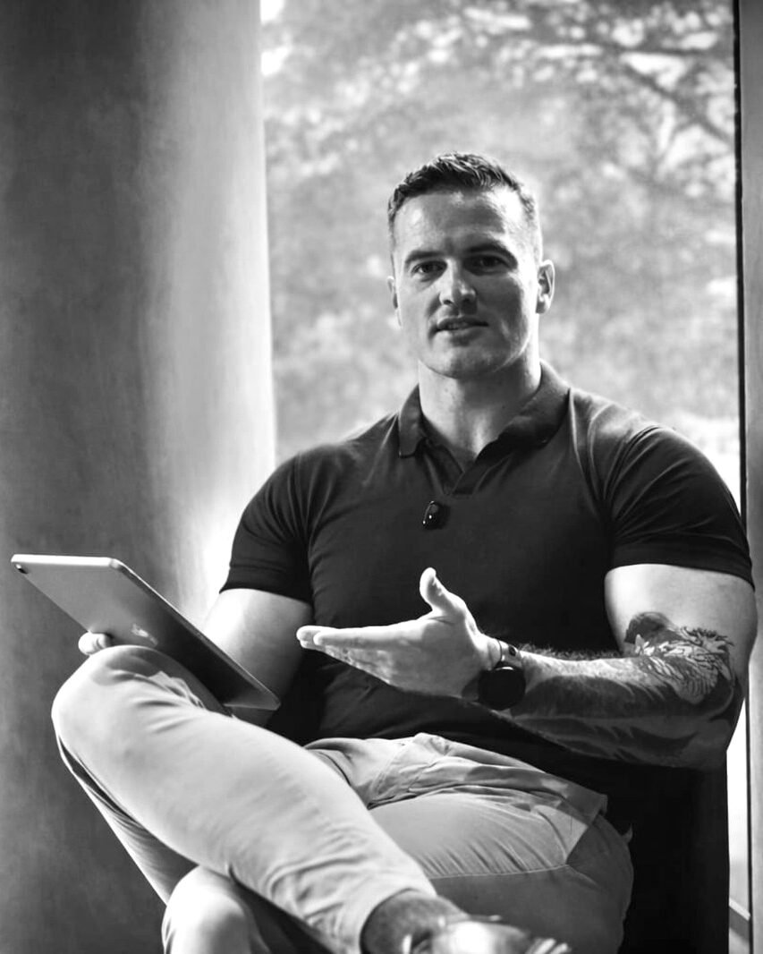 James Richman seated by a window, holding a tablet and speaking.
